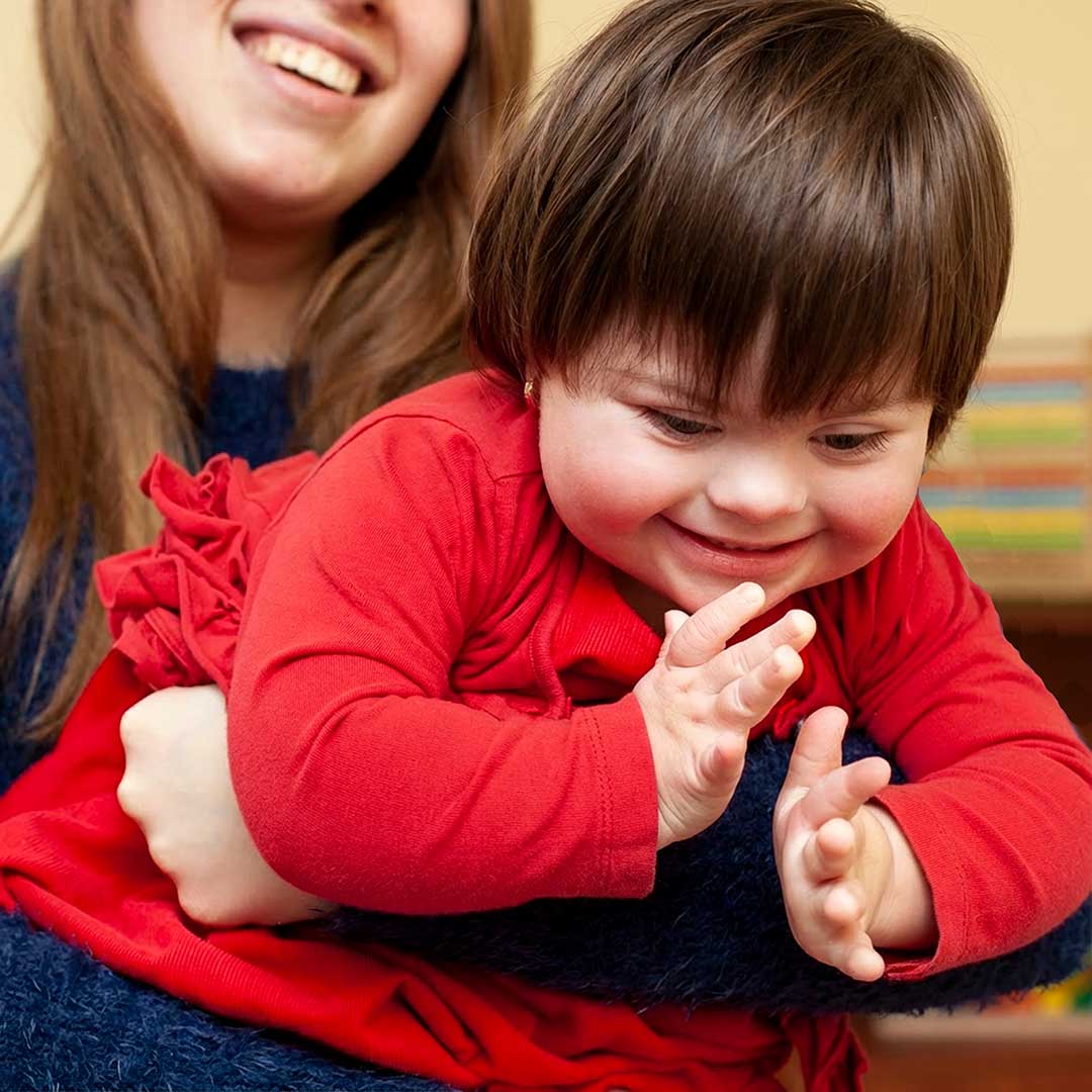 Parent helping a smiling child with down syndrome playing in a living room, representing the daily dedication of family caregivers.